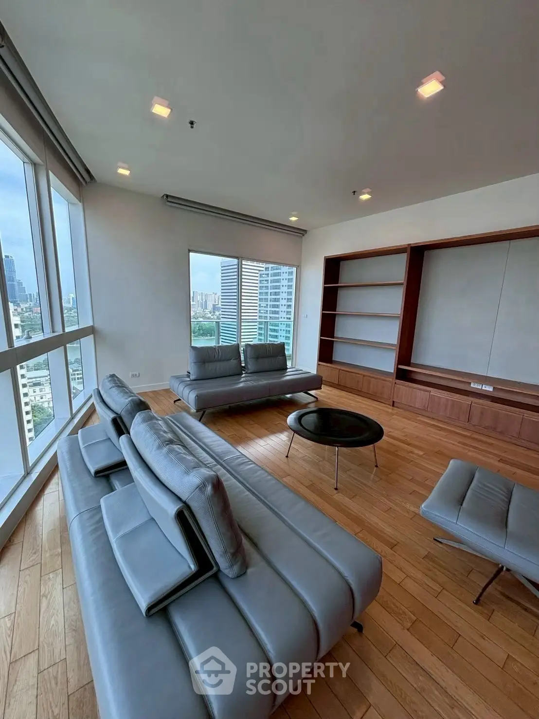 Spacious modern living room with city view, featuring sleek leather sofas and wooden flooring.