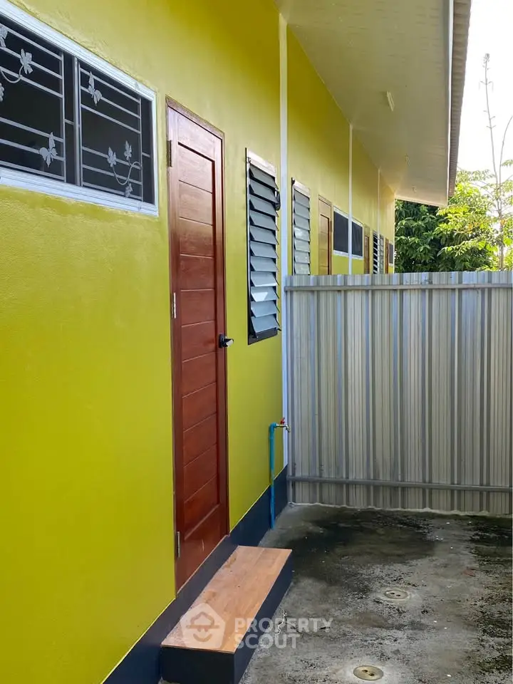 Vibrant yellow exterior of a modern building with wooden door and metal fence.