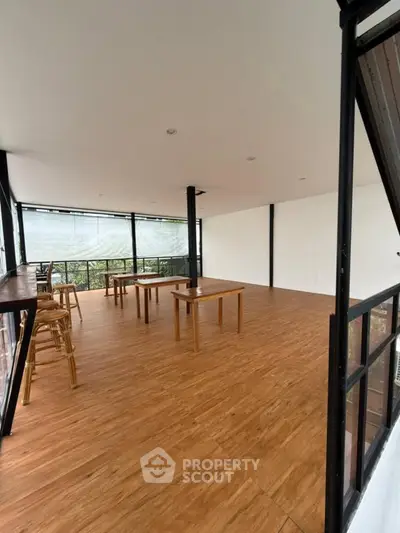 Spacious modern room with wooden flooring and large windows offering natural light