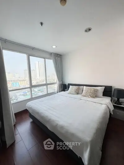 Spacious bedroom with large windows offering stunning city views, featuring a cozy bed and elegant decor.