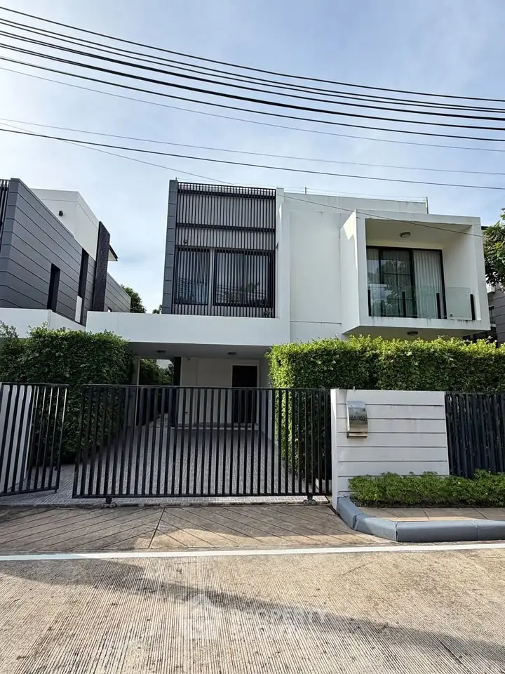 Modern two-story house with sleek design and gated entrance, surrounded by lush greenery.