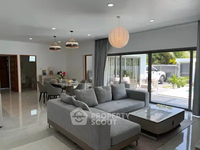 Spacious modern living room with open layout and pool view, featuring elegant gray sofa and stylish lighting.