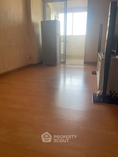 Spacious living area with wooden flooring and natural light from large window.
