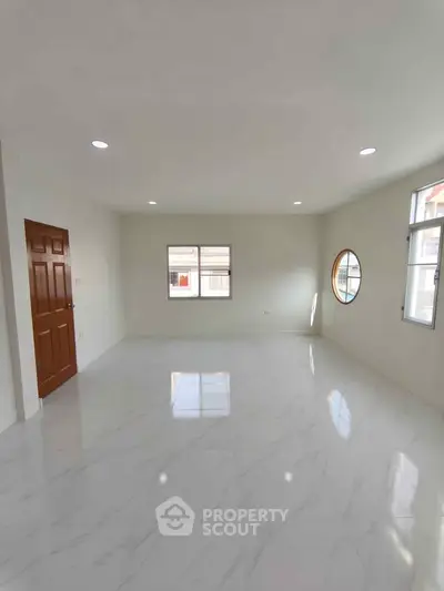 Spacious empty room with marble flooring and natural light from multiple windows.