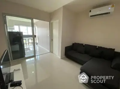 Modern living room with sleek sofa and air conditioning, adjacent to a bright kitchen area.