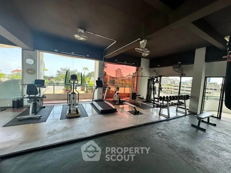 Spacious gym with modern equipment and city view in luxury apartment building.