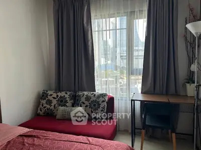 Cozy bedroom with city view, featuring a red sofa, desk, and large window with curtains.