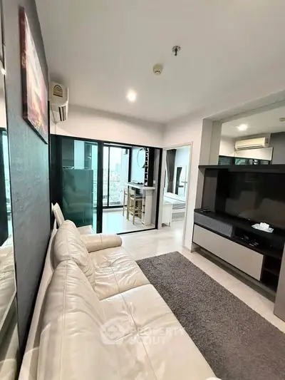 Modern living room with white leather sofa and large TV, featuring a view of the city through glass doors.