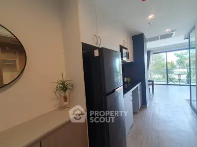 Modern kitchen with sleek black fridge and open layout leading to balcony with garden view.