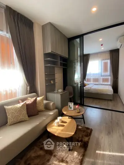 Modern living room with cozy sofa and stylish decor leading to a bright bedroom through glass doors.