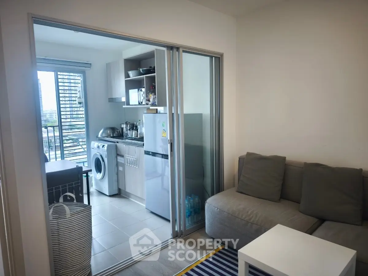 Modern apartment with open kitchen and cozy living area, featuring a washing machine and fridge.