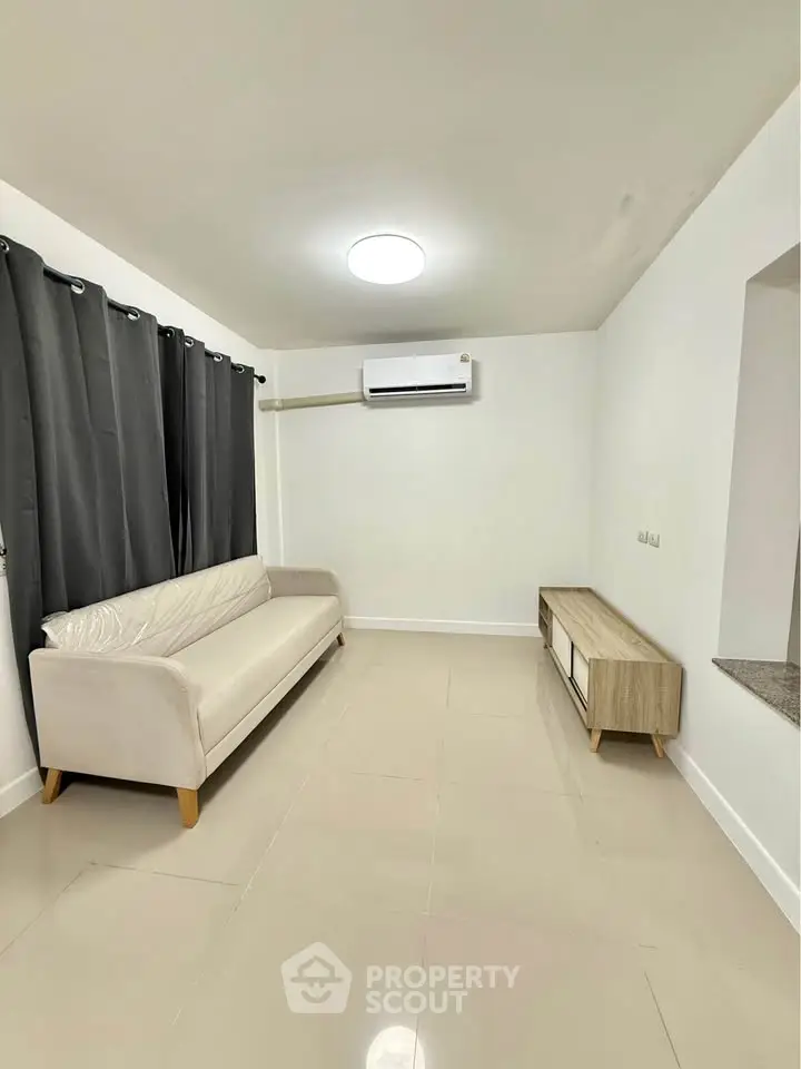 Spacious living room with modern sofa and air conditioning, ideal for relaxation.
