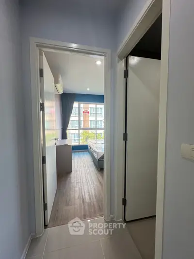 Modern apartment hallway leading to a bright bedroom with large window view.