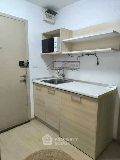 Compact kitchen with light wood cabinets and modern appliances in a cozy apartment.