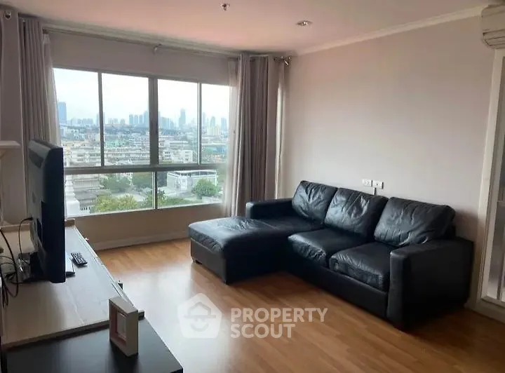 Spacious living room with large window offering stunning city views and modern black leather sofa.