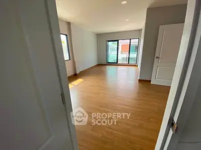 Spacious empty room with wooden flooring and large windows offering natural light.