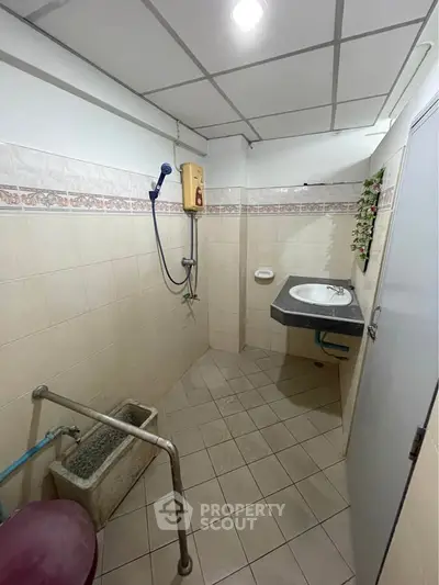 Compact bathroom with tiled walls and floor, featuring a wall-mounted sink and shower area.