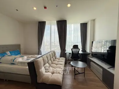 Modern studio apartment with city view, featuring a cozy bed, stylish sofa, and sleek entertainment unit.