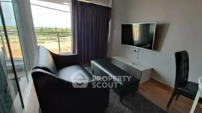 Modern living room with sleek black sofa and flat-screen TV, featuring a balcony view.