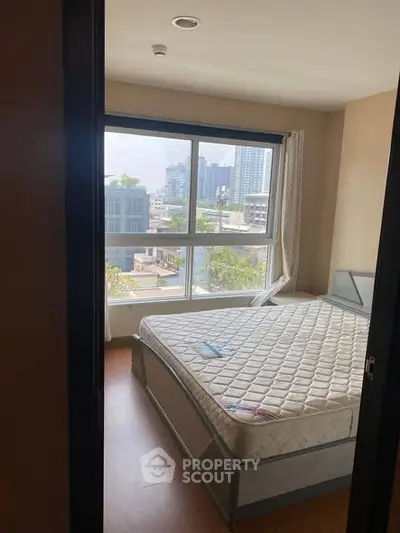 Spacious bedroom with large window offering city views, featuring a comfortable bed and modern decor.