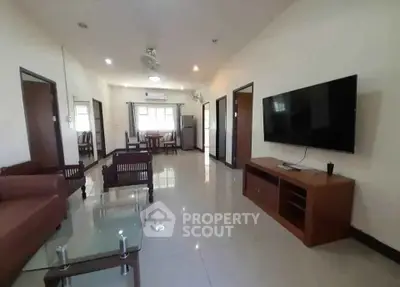 Spacious living room with modern furniture and large TV, leading to a dining area and kitchen.