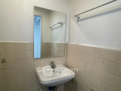 Compact bathroom with wall-mounted sink and mirror, featuring tiled walls and towel rack.