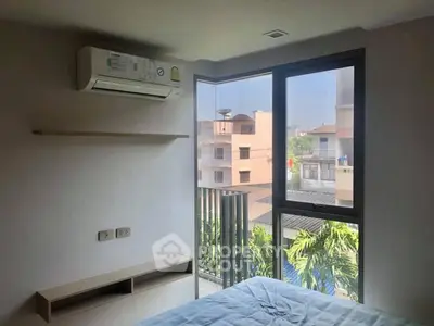 Cozy bedroom with large window and air conditioning, offering a pleasant view of the neighborhood.