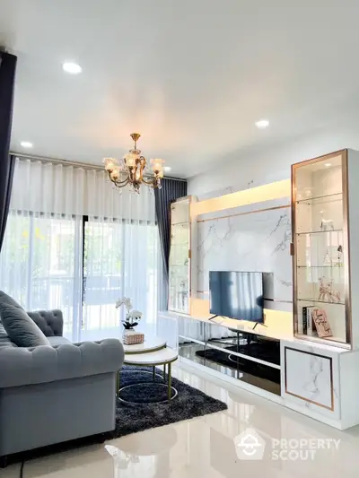 Elegant living room with luxurious marble TV wall, plush seating, and chic chandelier, opening to a sunlit balcony through sheer curtains.