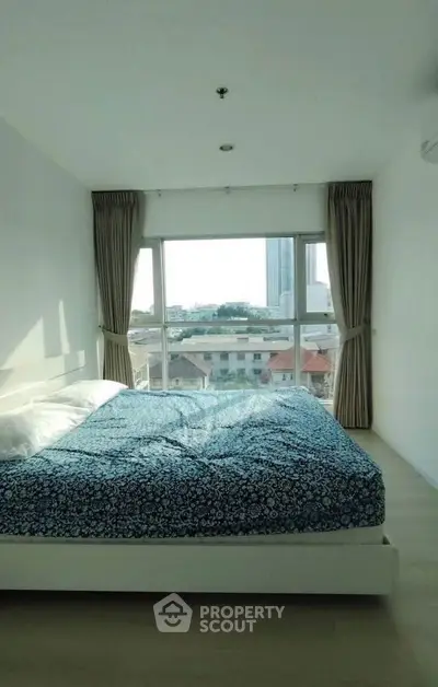 Bright bedroom with large window offering city view, featuring a cozy bed and modern decor.