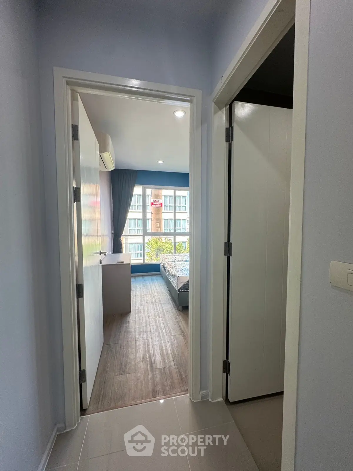 Modern apartment hallway leading to a bright bedroom with large window view.