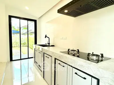 Modern kitchen with sleek design and gas stove, featuring large windows for natural light.