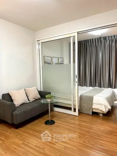 Modern studio apartment with cozy living area and stylish bedroom separated by glass sliding door.