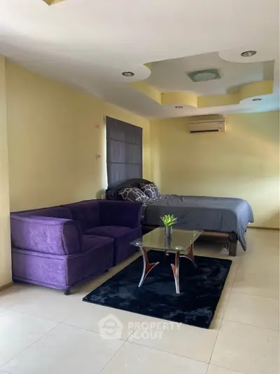 Cozy bedroom with modern decor, featuring a plush purple sofa and stylish glass coffee table.