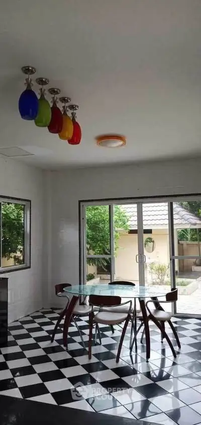 Chic dining area with colorful pendant lights and glass table, overlooking a serene garden.