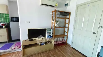Cozy living room with wooden flooring, TV stand, and open shelving, adjacent to a compact kitchen.