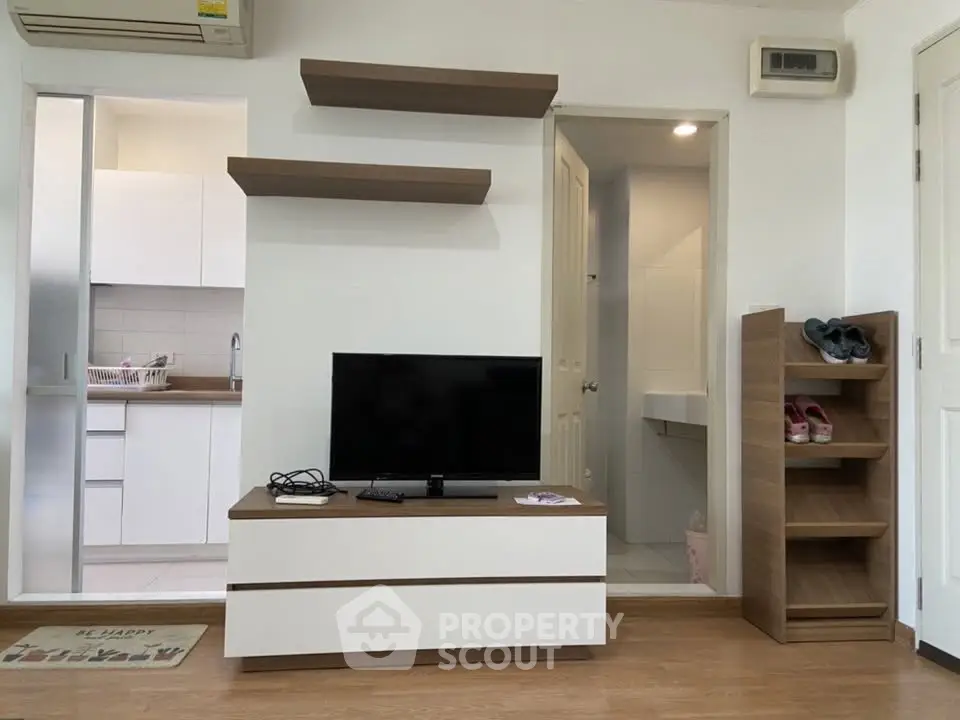 Modern living room with TV, open kitchen, and stylish shelving in a cozy apartment.