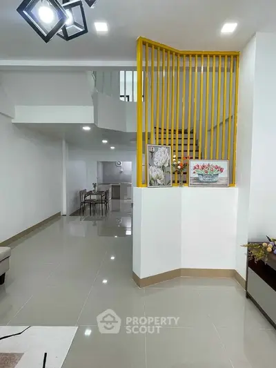 Modern open-plan living area with stylish staircase and dining space, featuring sleek tile flooring and contemporary lighting.