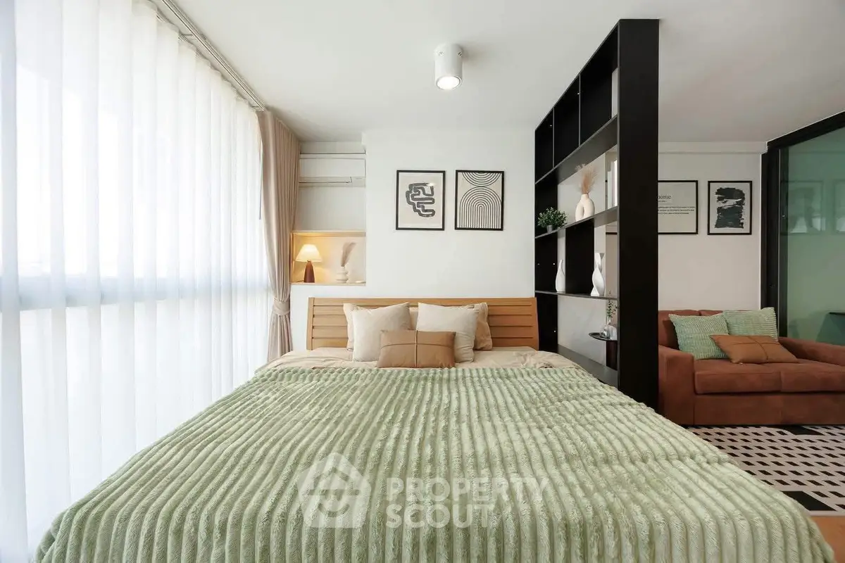 Modern bedroom with stylish decor and cozy seating area, featuring a large window with sheer curtains.