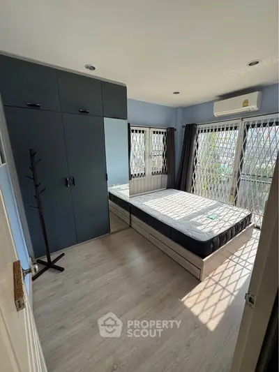 Bright bedroom with large windows and modern furnishings, featuring a spacious wardrobe and air conditioning.