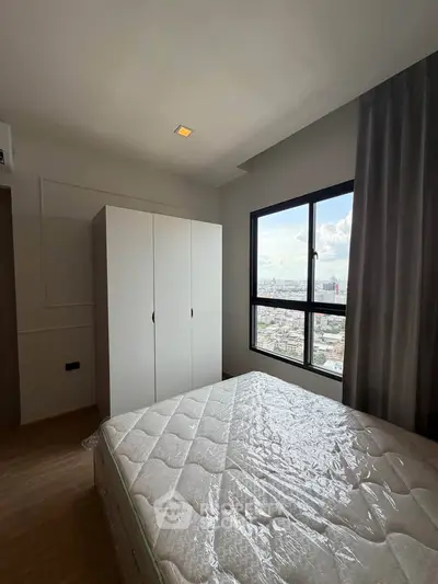 Spacious bedroom with large window offering stunning city views, featuring a comfortable bed and ample storage.