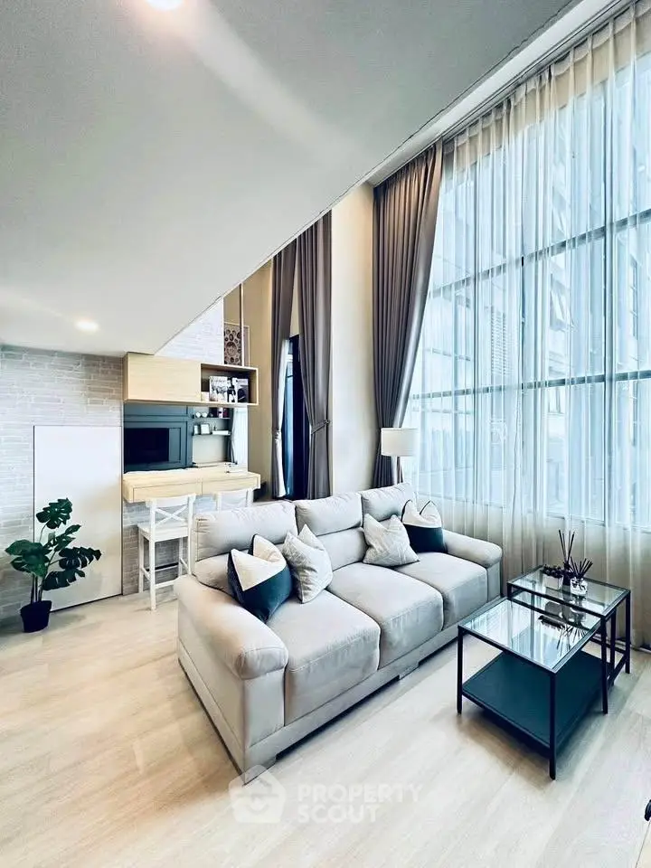 Spacious modern living room with high ceilings and large windows, featuring a cozy sofa and elegant decor.