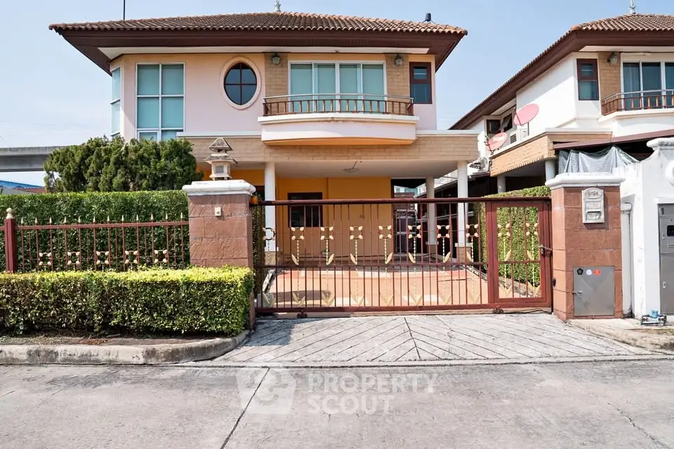 Charming two-story house with gated entrance and lush greenery in suburban neighborhood.