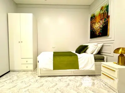 Modern bedroom with white furniture and green accents, featuring a stylish painting and elegant lighting.