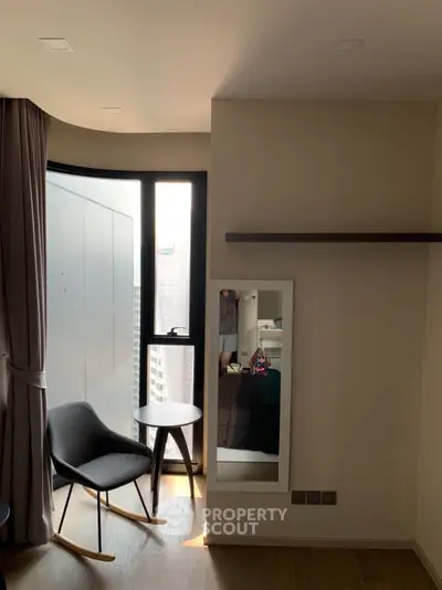 Modern apartment corner with chair, table, and mirror reflecting city view.