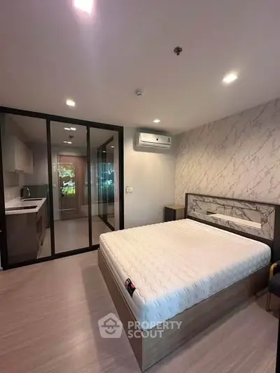 Modern bedroom with glass partition and sleek kitchen area, featuring stylish decor and ample natural light.