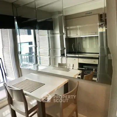 Modern kitchen with sleek cabinetry and dining area, featuring a reflective backsplash and natural light.