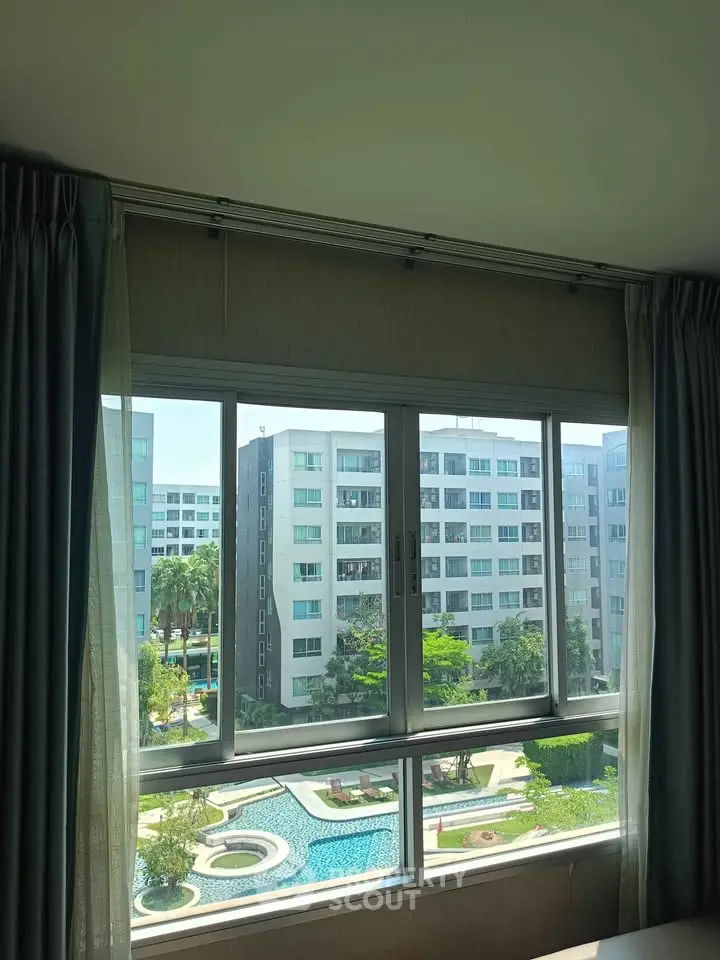 Spacious apartment with large window offering stunning view of modern buildings and lush greenery.