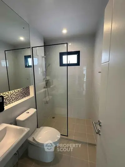 Modern bathroom with glass shower, sleek fixtures, and neutral tiles.