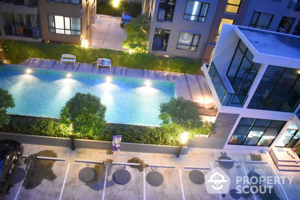 Modern apartment complex with illuminated pool and parking area at night