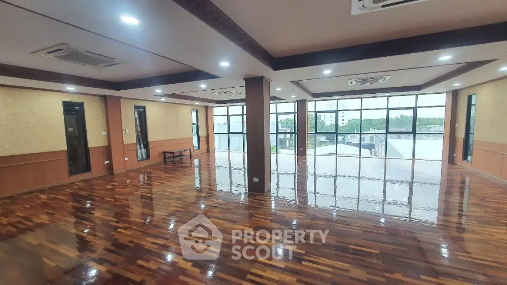 Spacious open-plan room with polished wooden floors and large windows offering natural light and city views.